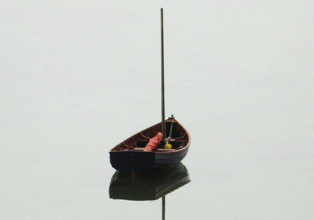 Solitary boat floats on calm water with a perfect reflection, creating a serene and tranquil scene.