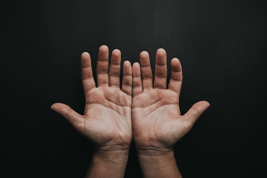 A pair of upturned hands displayed against a dark background, showcasing skin texture.